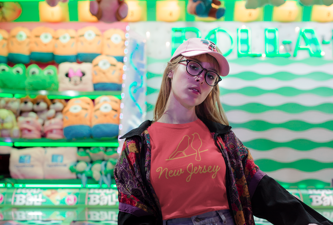 Person holding a pink plush toy in front of a colorful arcade setting with a New Jersey birds tee shirt on